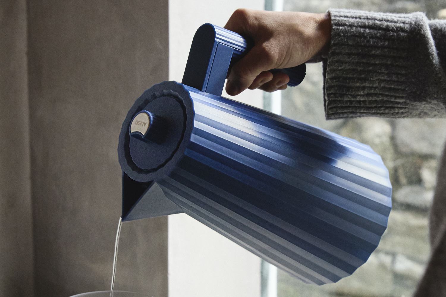 Blauer Alessi Plissé Wasserkocher beim Ausgießen von Wasser, modernes Küchendesign.