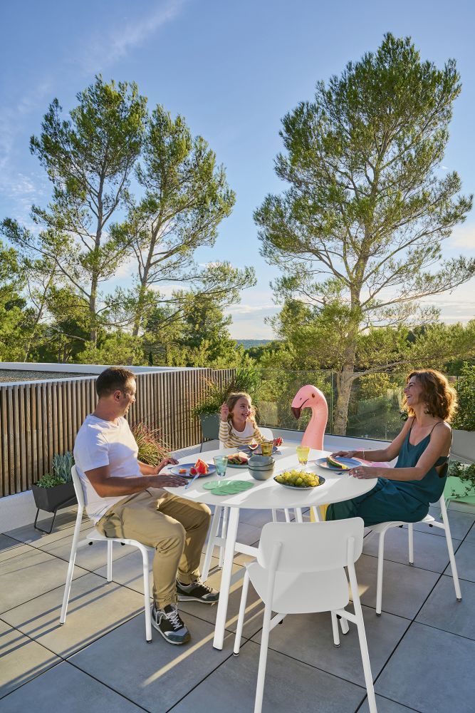 Familie genießt Mahlzeit am weißen SO´O Esstisch von Fermob im Freien auf der Dachterrasse.
