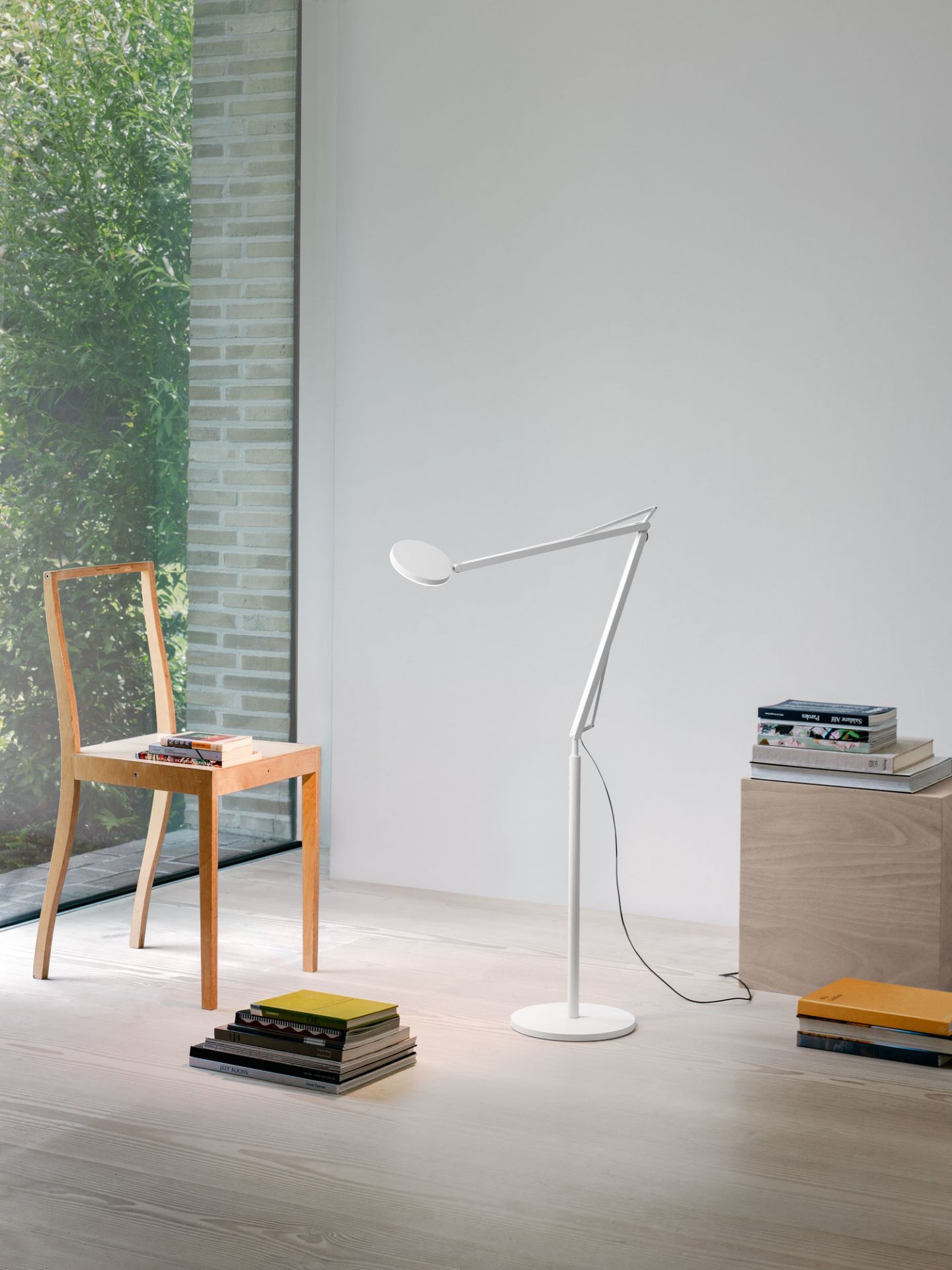 Moderne, graue Stehleuchte "John" im minimalistischen Wohnzimmer mit Bücherstapeln und Stuhl. Design Lampe für Wohnraumbeleuchtung.