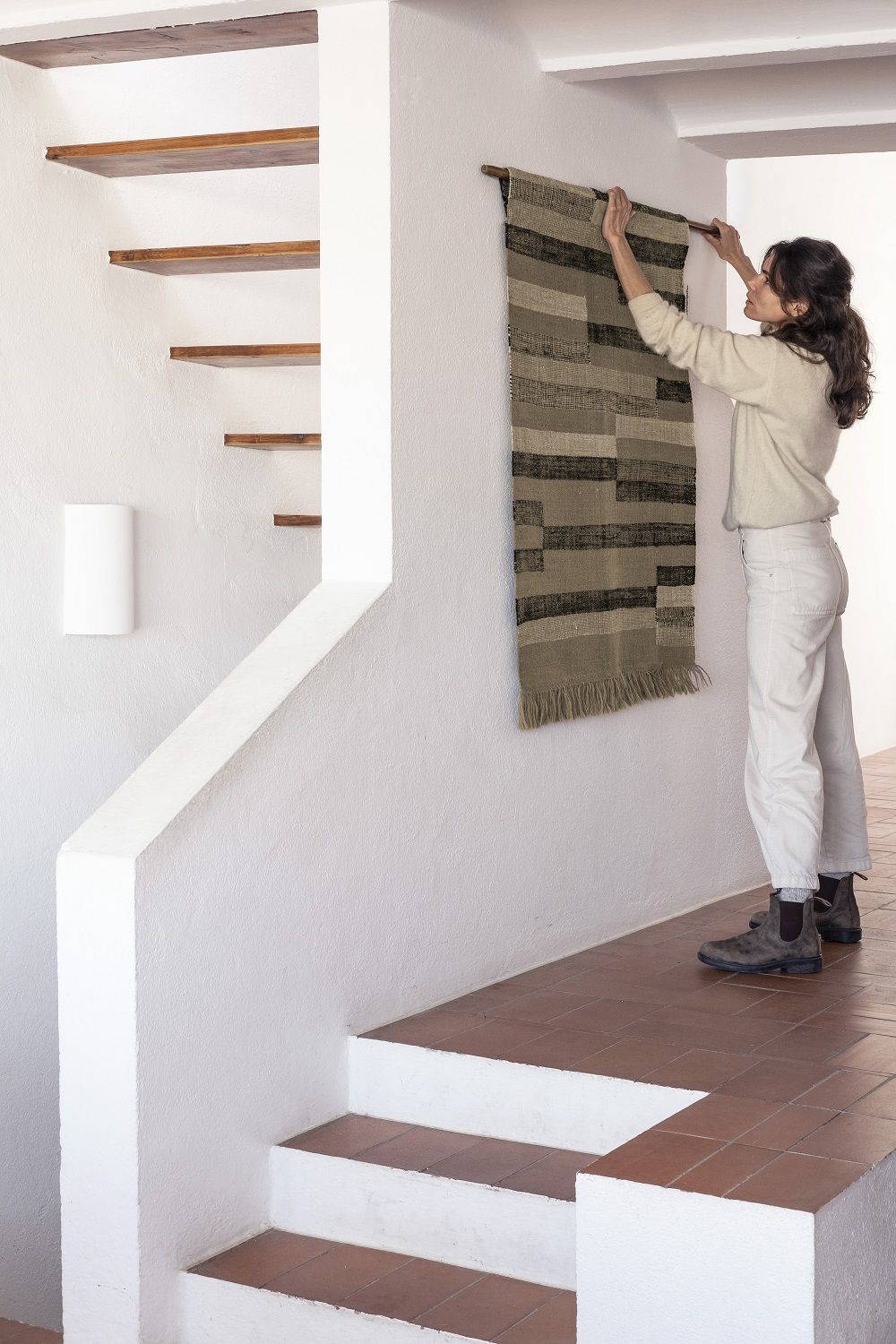 Frau hängt Nanimarquina Improvisation Tapisserie an weiße Wand. Moderne Wandteppich Kunst für Zuhause.