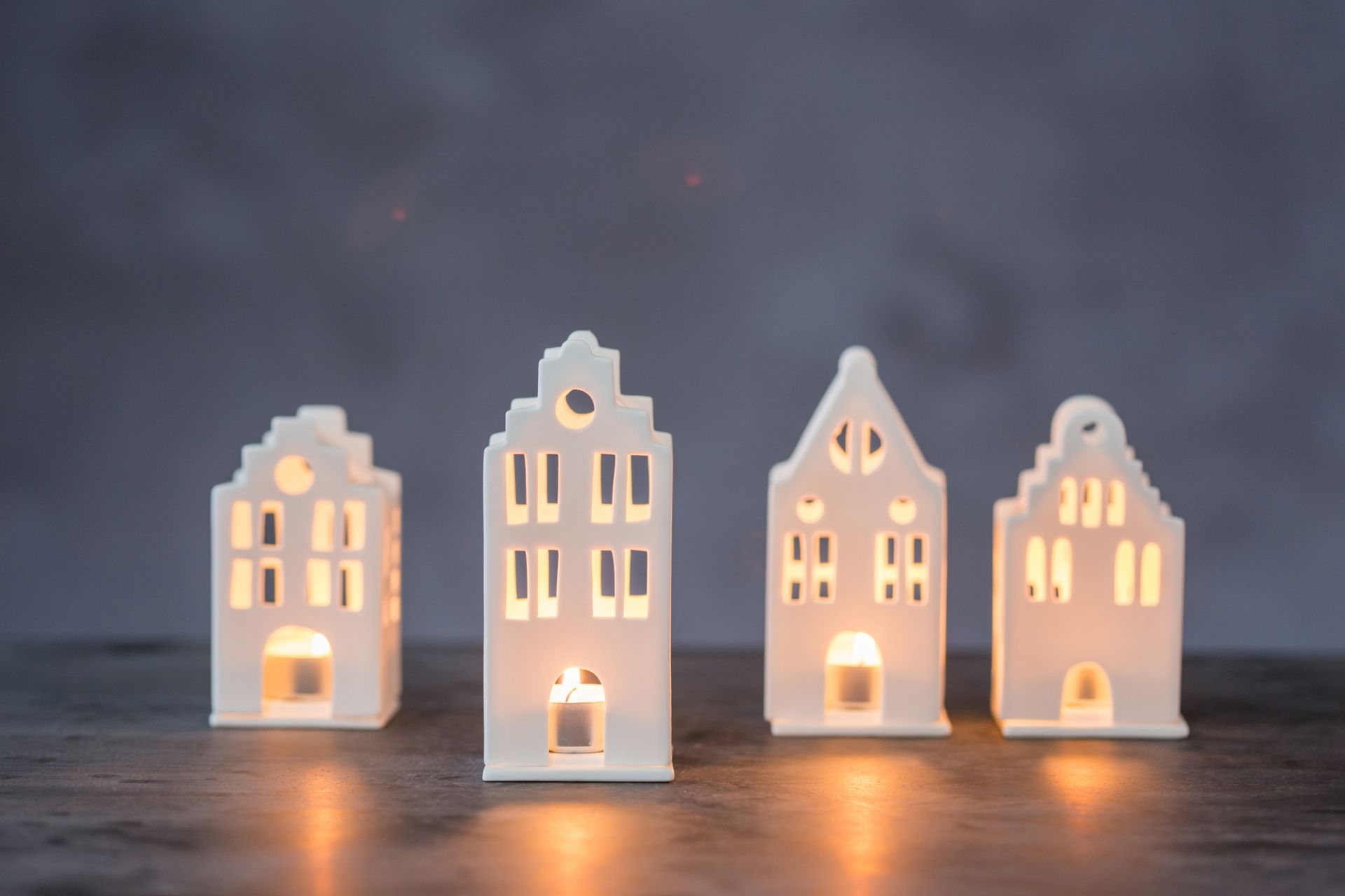 Vier weiße Mini Lichthäuser im Giebelhaus-Stil mit warmem Kerzenlicht für gemütliche Wohnraumdekoration.