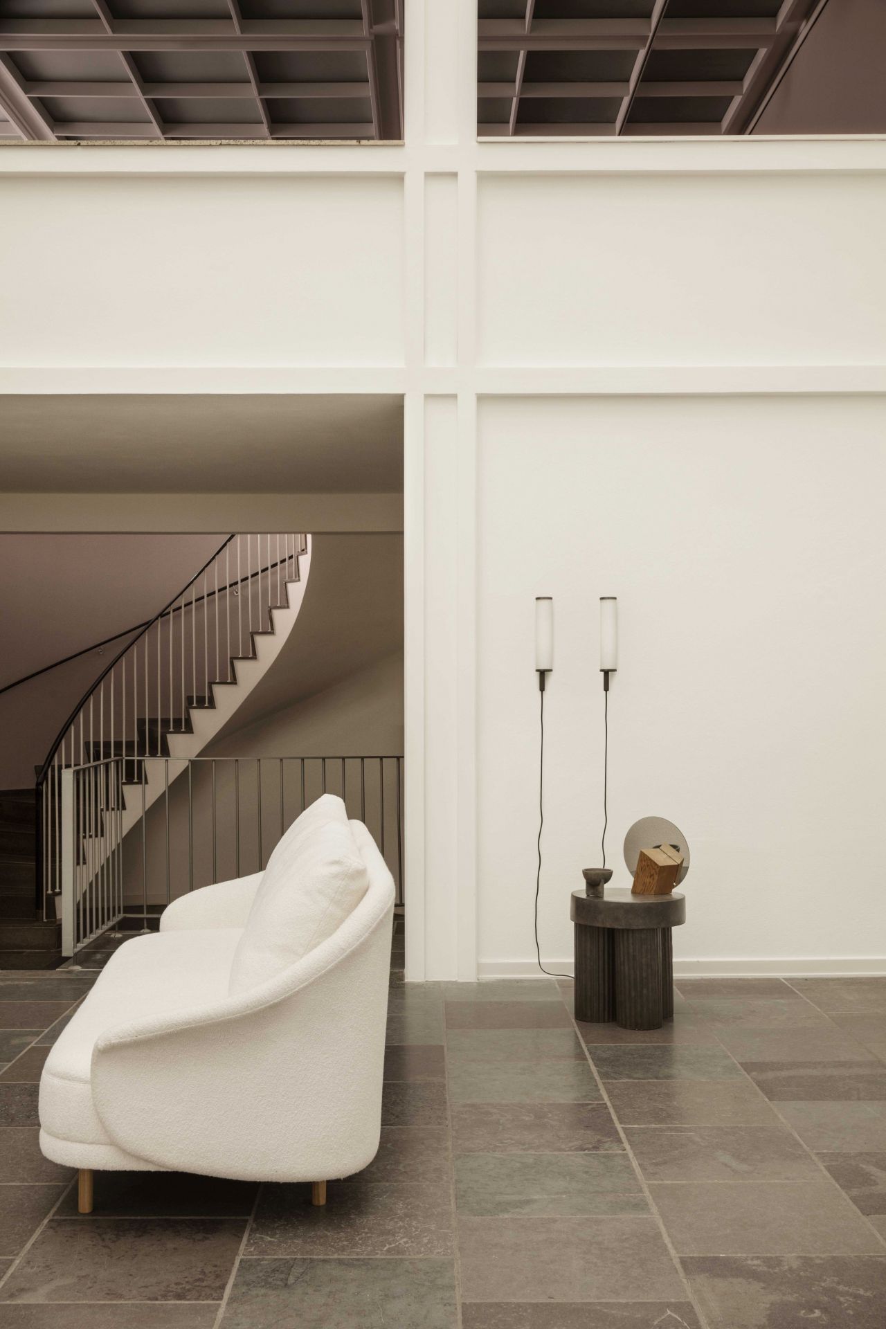 Norr11 Gear Beistelltisch aus Travertin neben einem weißen Sofa in einem minimalistischen Interieur.