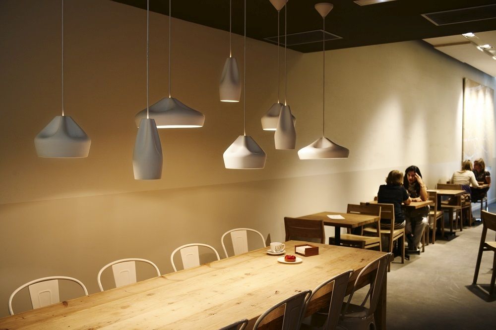 Pleat Box Pendelleuchten in Grau und Gold über einem langen Holztisch in einem Restaurant.