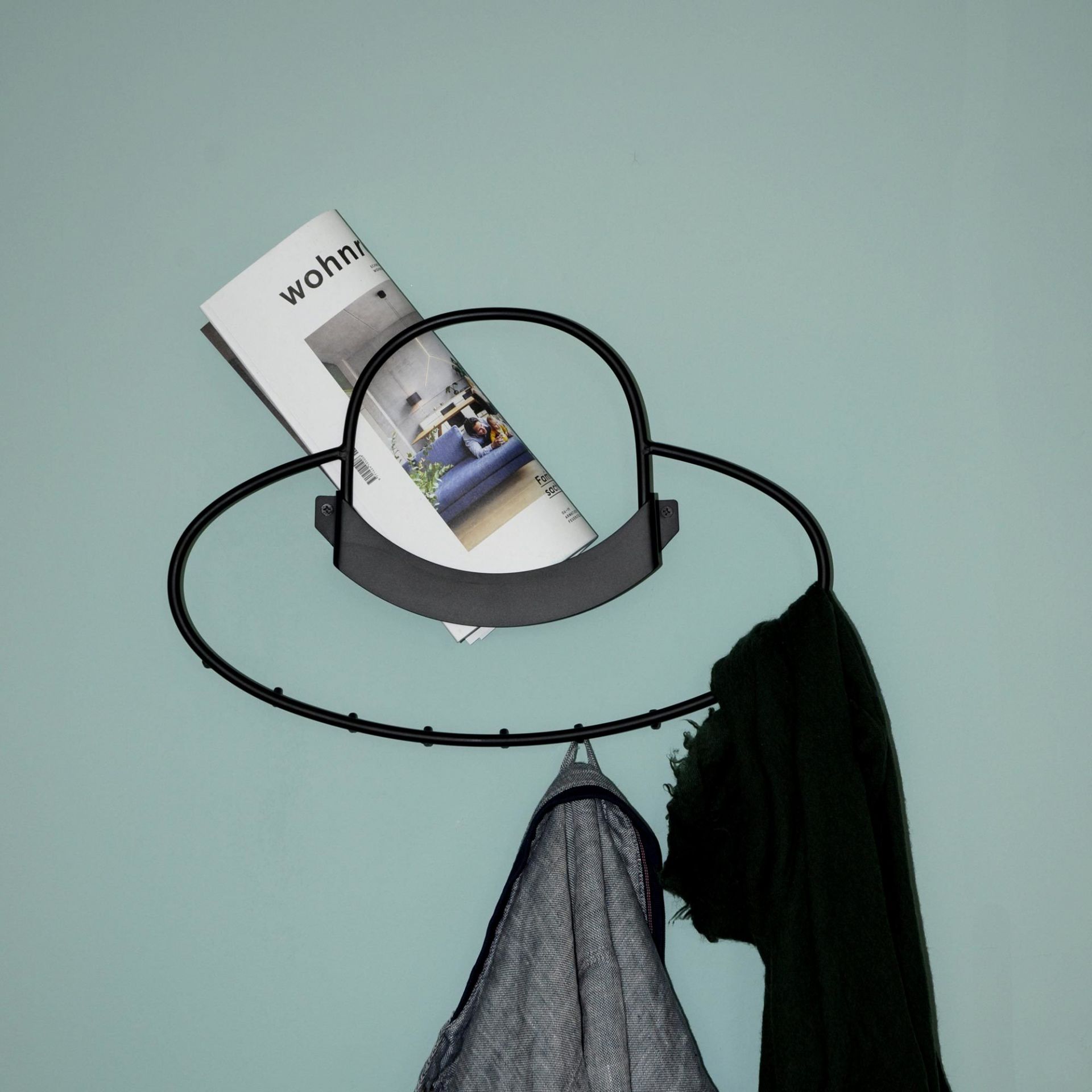 Schwarze Hat Wandgarderobe mit Haken, Jacke, Schal und Magazin an hellblauer Wand.