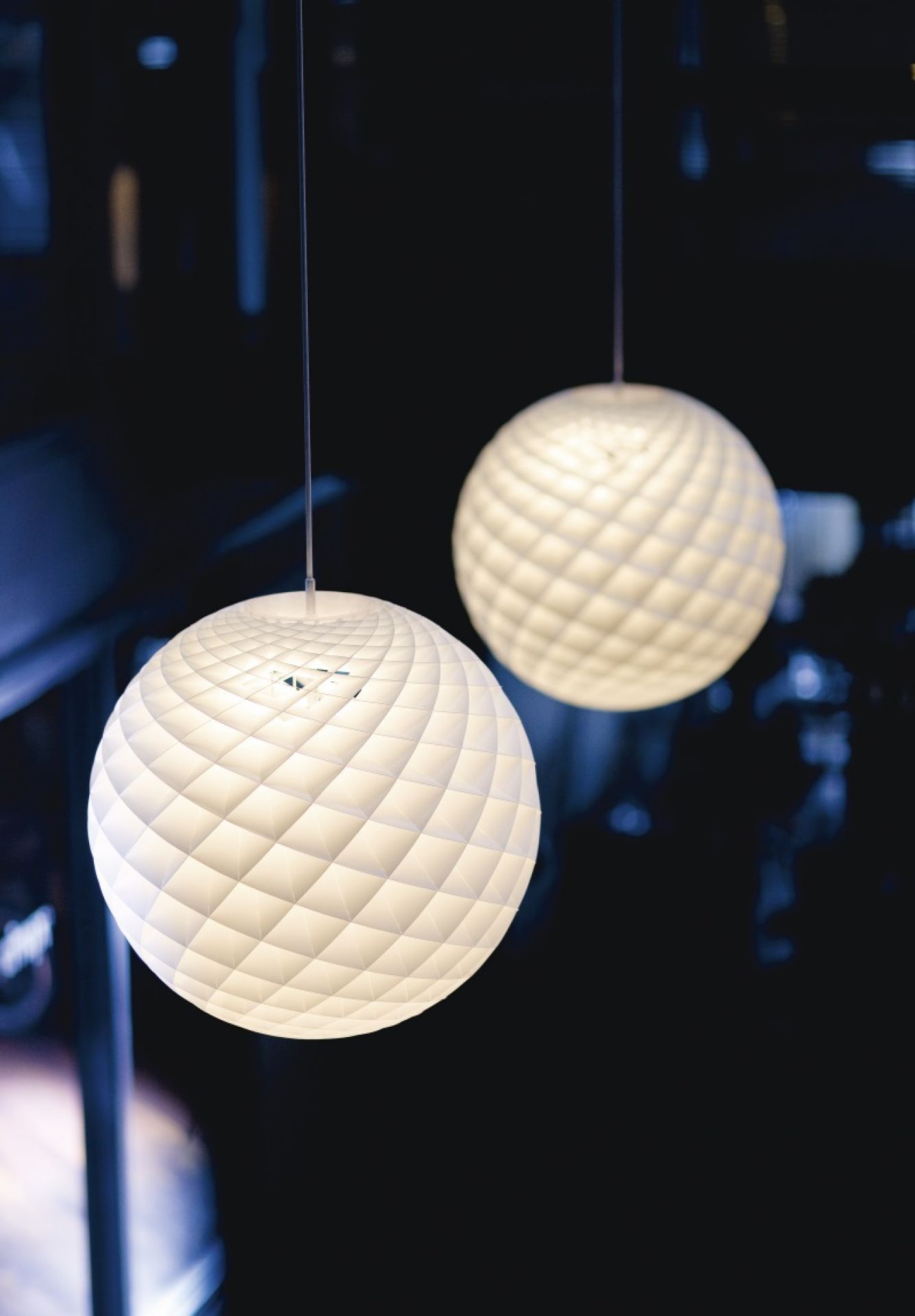 Zwei Patera Pendelleuchten von Louis Poulsen, kugelförmig mit geometrischem Muster, hängen im Raum.