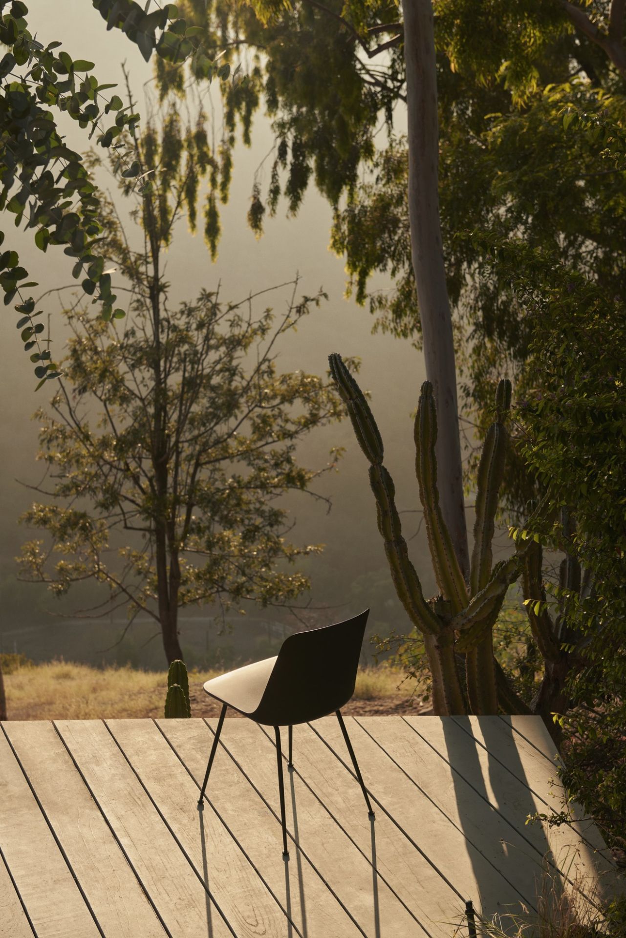 Schwarzer AndTradition Rely HW70 Outdoor Stuhl auf Holzterrasse vor Bäumen und Kakteen.