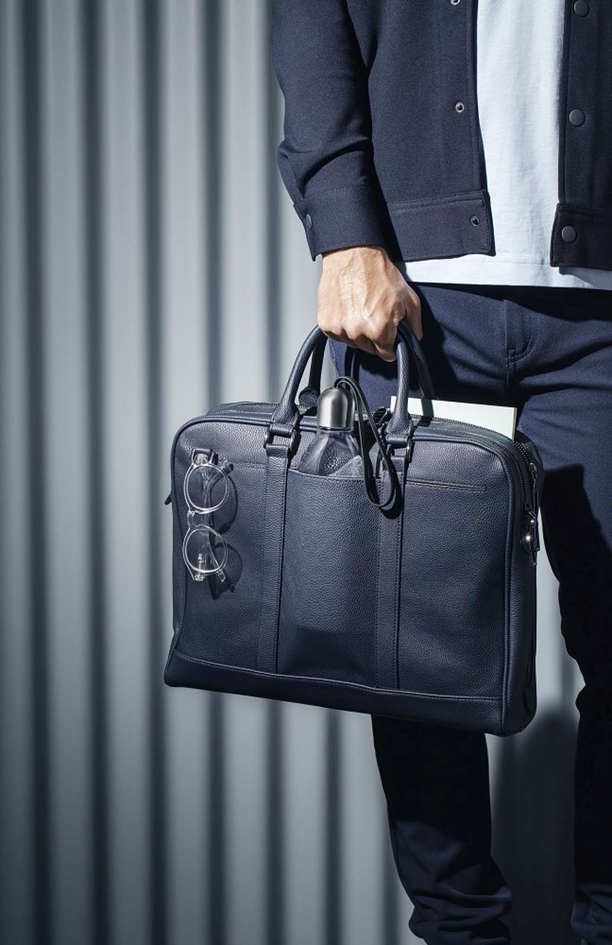 Mann hält schwarze Aktentasche mit Eva Solo Trinkflasche und Brille. Stilvolles Accessoire für Büro und Freizeit.