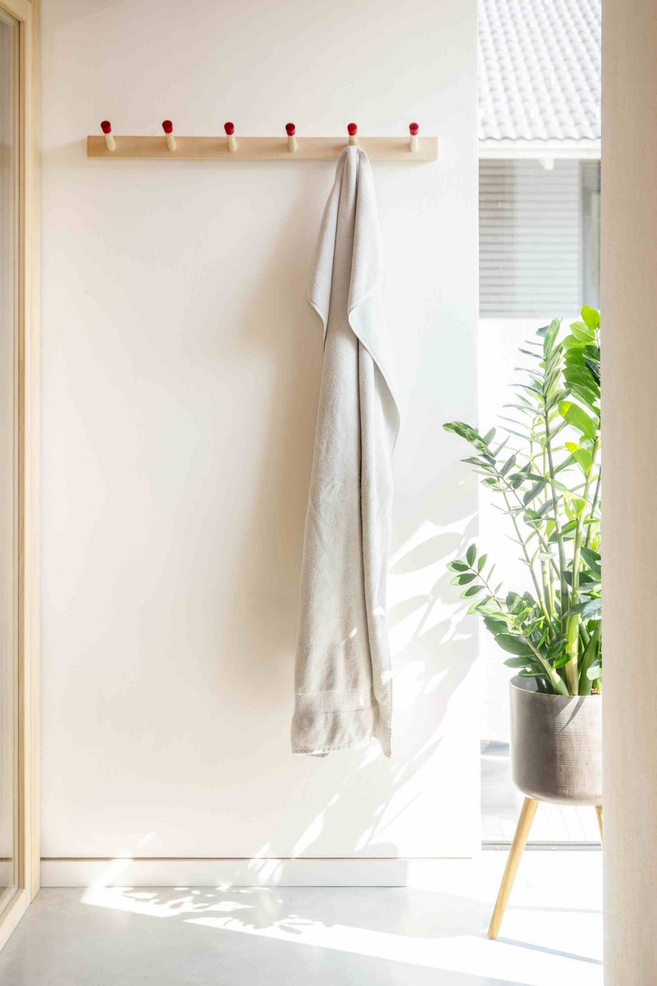 Helle Holz Hakenleiste von Moormann mit roten Akzenten und Handtuch an weißer Wand.